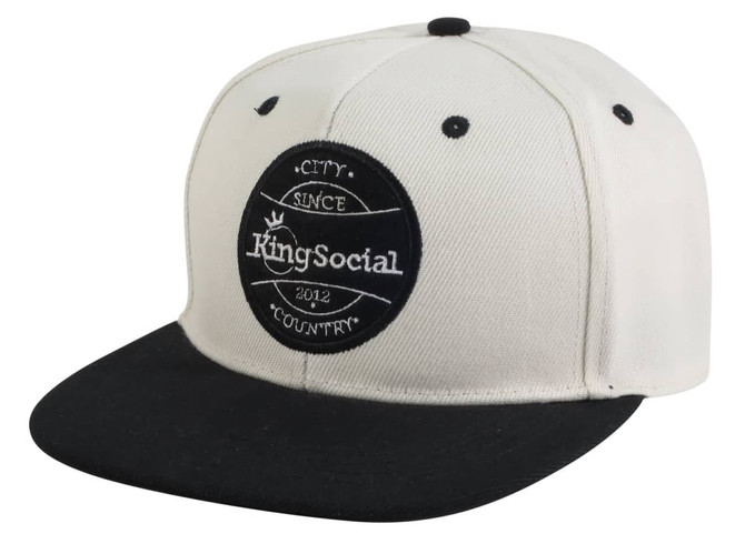 A flat peak cap with a cream-coloured crown and a black peak, featuring a logo on the front.