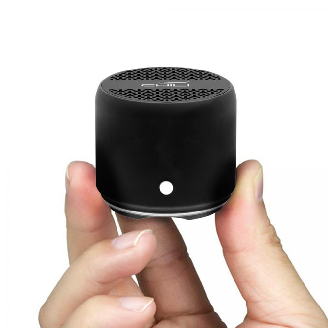 A compact black Bluetooth speaker held in a hand, featuring a textured top and a small logo.