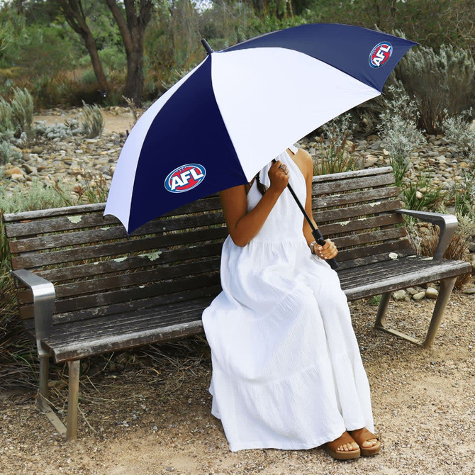 A navy and white umbrella featuring a logo, held by a person in a white dress, seated on a wooden bench.