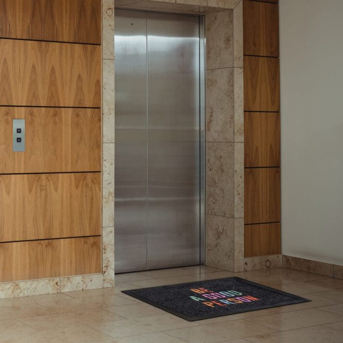 A nylon floor mat in front of a sleek elevator, featuring a logo and multicoloured text on a dark background.