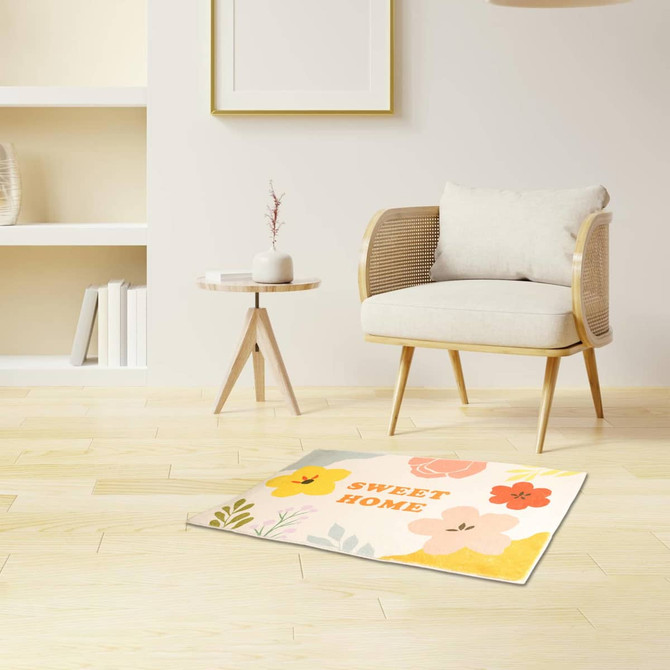 A plush logo mat featuring colourful floral designs, placed on a wooden floor next to a minimalist chair and table.