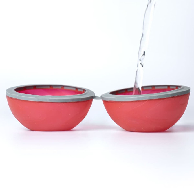 A red and grey reusable water balloon split in half, with water being poured into one half.