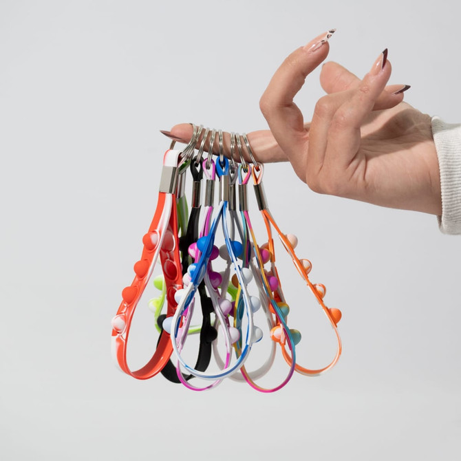 A hand holding multiple Popper Stress Reliever Key Chains in various bright colours. The keychains include a variety of playful designs.