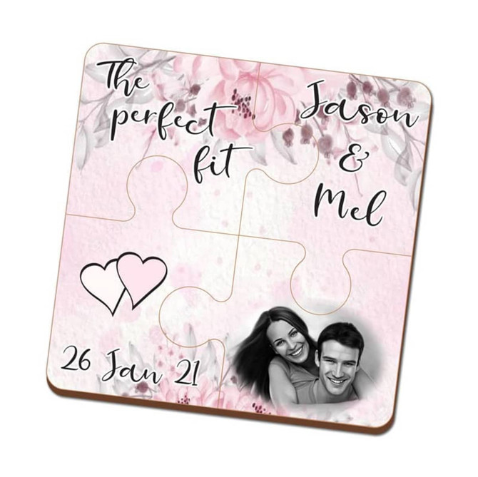 A pink four-piece MDF coaster puzzle featuring floral designs, two names, and a heart graphic. Includes a logo.