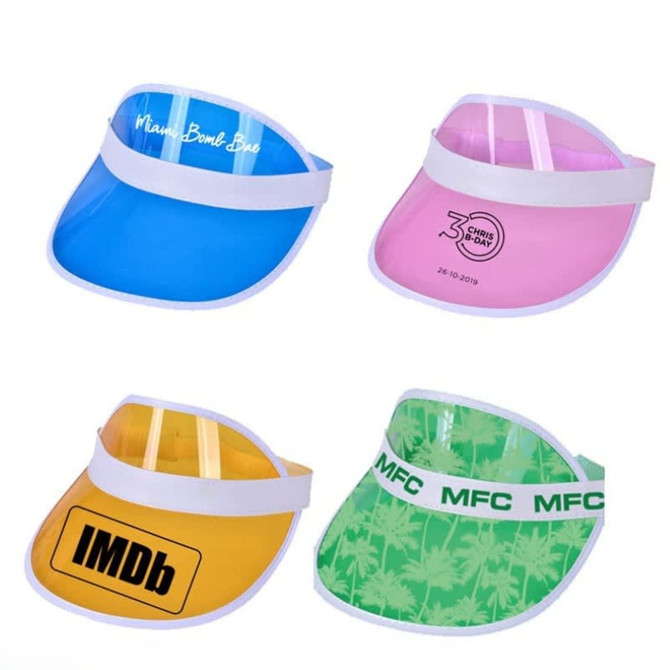 Four PVC sun visors in blue, pink, yellow, and green, featuring various designs and logos.