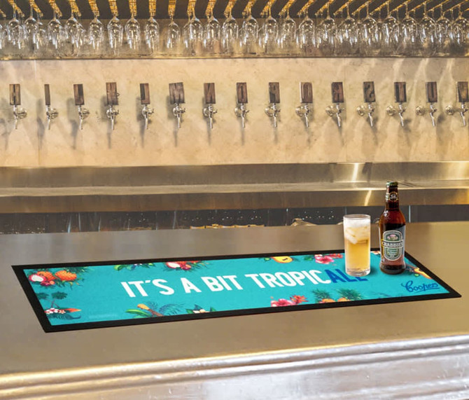 A bar runner in vibrant teal featuring tropical designs, placed on a polished bar with drinks nearby.