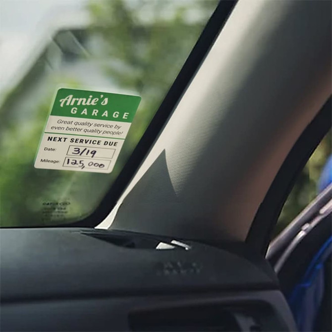 A service sticker featuring green and white design, attached to a car window, indicating service details.