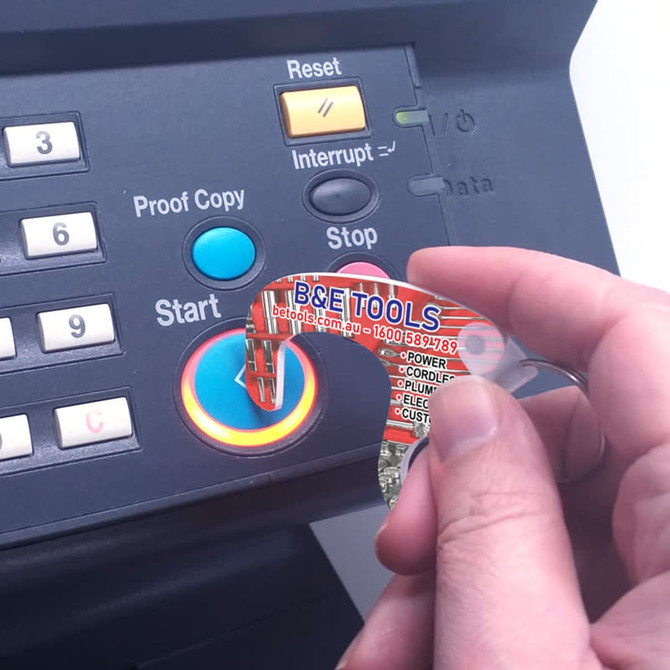 A transparent tool with an orange design, being used to press a button on a machine. It has a logo.