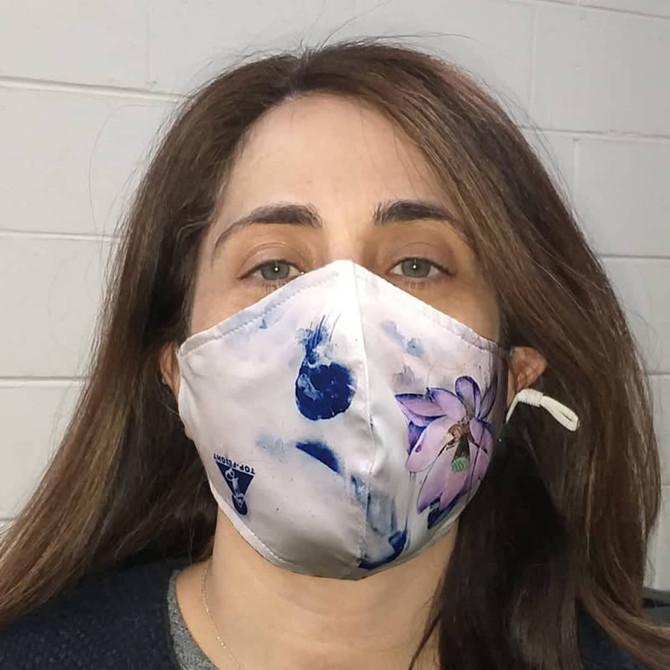 A fabric face mask with a floral design in pastel colours, featuring a logo on one side.