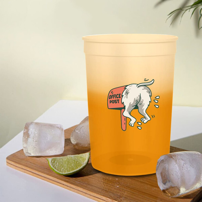 A colour-changing plastic stadium cup in a yellow-orange hue, featuring a logo and placed on a wooden surface with ice and lime.