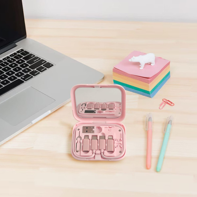 A pink charging data cable kit in a compact case, featuring multiple cable connectors, placed next to a laptop and stationery.