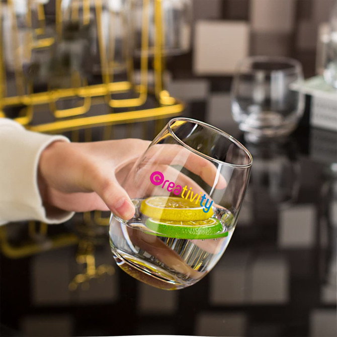 An egg-shaped glass cup held in a hand, filled with water and a slice of lime, featuring a logo.