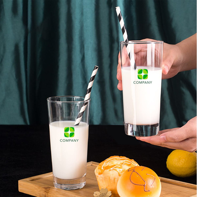 A clear glass with a black and white striped straw, filled with a white beverage, beside a similar glass and pastries.