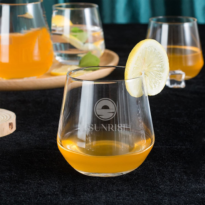 A wine glass filled with orange liquid, garnished with a slice of lemon, with additional glasses in the background.