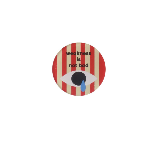 An acrylic fridge magnet featuring a striped design with an eye illustration, displaying the phrase "weakness is not bad."