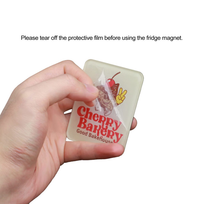 A hand holding a rectangular acrylic fridge magnet featuring a logo and design, with a protective film being peeled off.