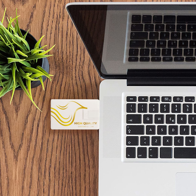 A credit card-sized Type-C flash drive in white connected to a laptop on a wooden desk with a small plant.