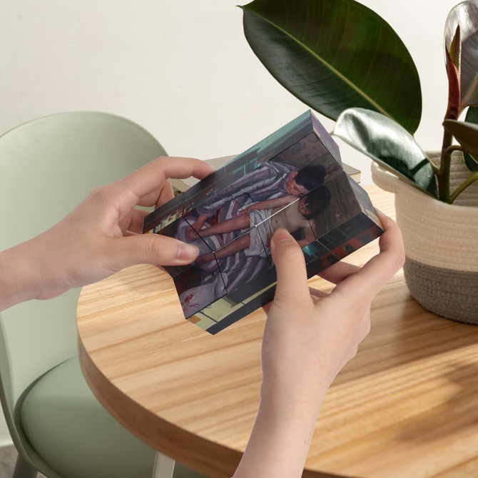 A hands holding a transparent 3D cube featuring colourful images on its sides, placed on a wooden table near a plant.