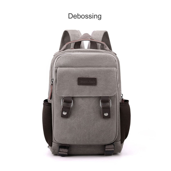 A grey canvas sling backpack with adjustable straps, featuring a front pocket and a logo.