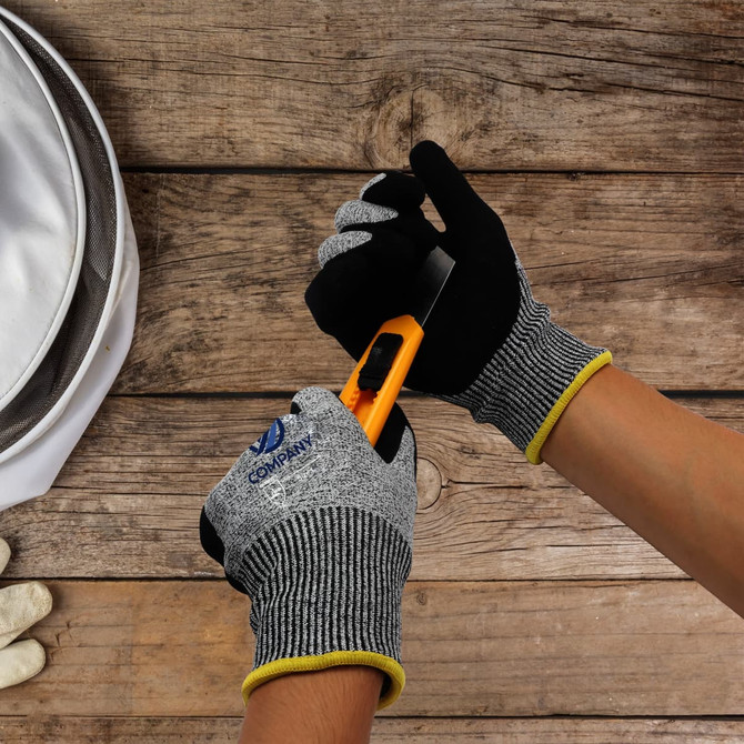 Cut resistant nitrile gloves in grey and black with a yellow cuff, being used to handle a utility knife.