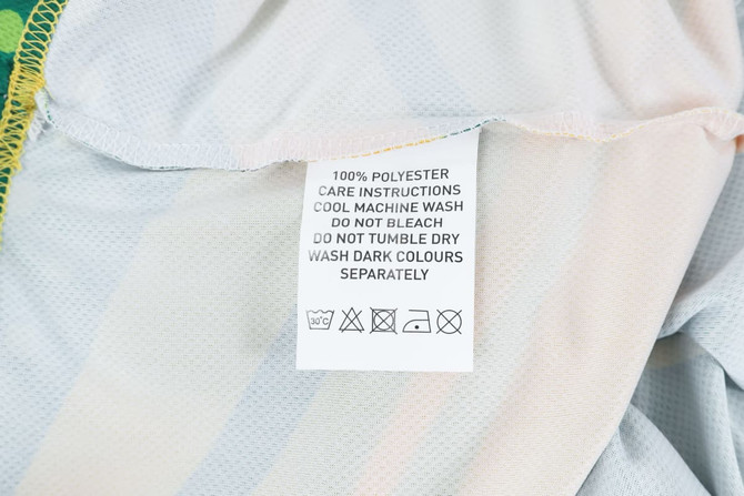 A care label on a 100% polyester micro mesh sports long sleeves shirt, featuring fabric care instructions.