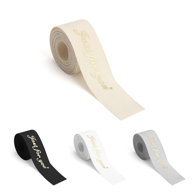 A roll of hot stamping cotton ribbon in cream, black, white, and grey, featuring a decorative printed text and branding.
