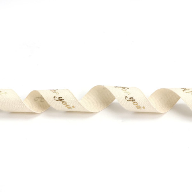 A wavy, cream cotton ribbon with hot stamping in gold. It features a decorative design and includes a logo.