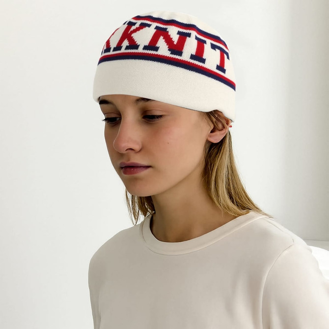 A cream-coloured beanie with red and blue stripes and a logo, worn by a person with long hair.