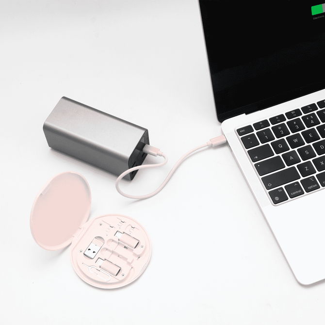 A silver power bank connected to a laptop, alongside a round, pink cable kit containing various connectors.