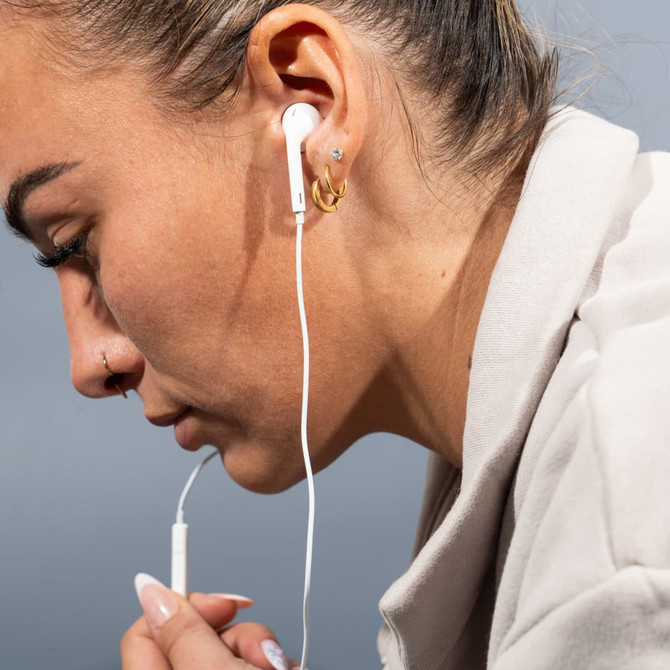 A woman with light skin has white USB Type C earphones in her ears, with soft lighting and a neutral background.