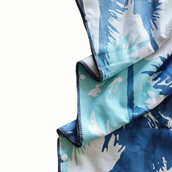 A hooded change towel in shades of blue and white with a palm leaf design, featuring a branded logo.