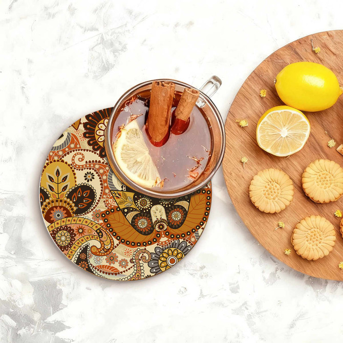 A round ceramic coaster featuring a colourful paisley design, with a drink and biscuits displayed alongside.