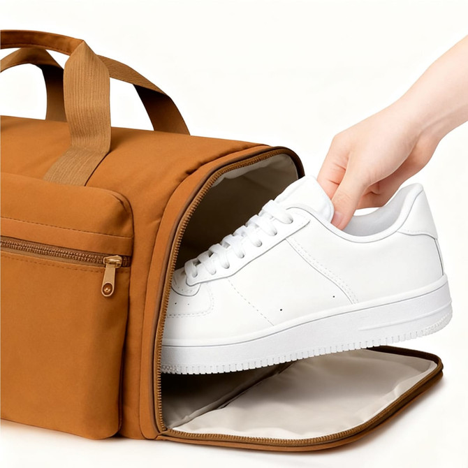A foldable travel duffle bag in brown, with a hand placing a white sneaker inside. It features a zippered compartment.
