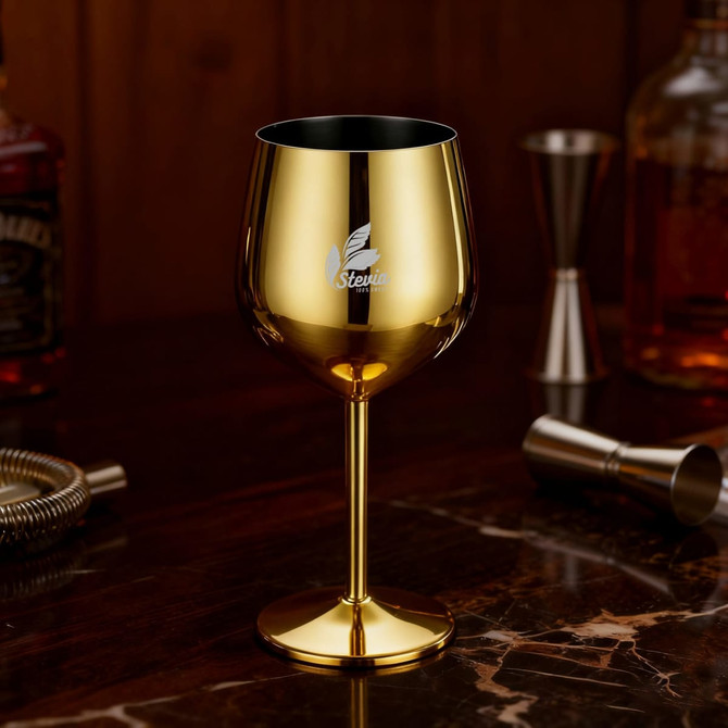 A stainless steel wine goblet in a shiny gold finish, featuring a logo, set on a marble table with bar accessories.
