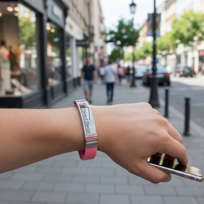 A metal bracelet in pink and silver is worn on a wrist, with a street scene in the background.