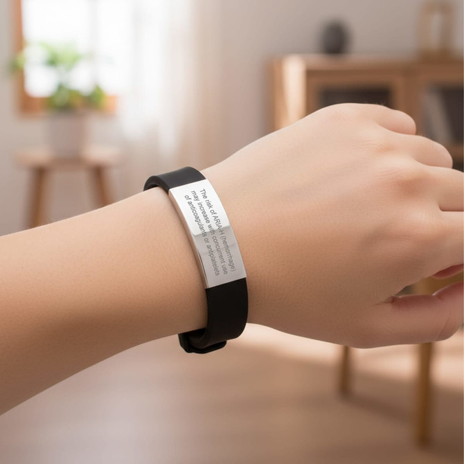 An engraved stainless steel bracelet with a black strap, displayed on a hand in a bright indoor setting.