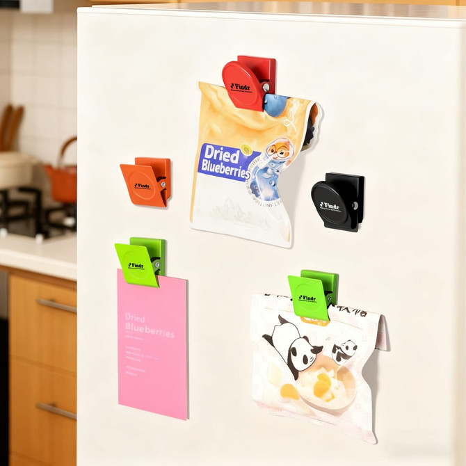 A set of metal magnetic clips in green, orange, black, and red attached to a fridge, holding various items.
