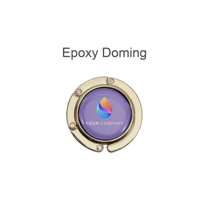 A round, foldable desk hook in gold with a purple center featuring a logo.