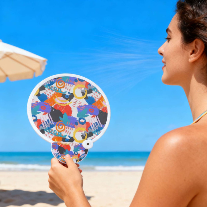 A colourful 20cm foldable fan featuring a vibrant design, held by a person at the beach.