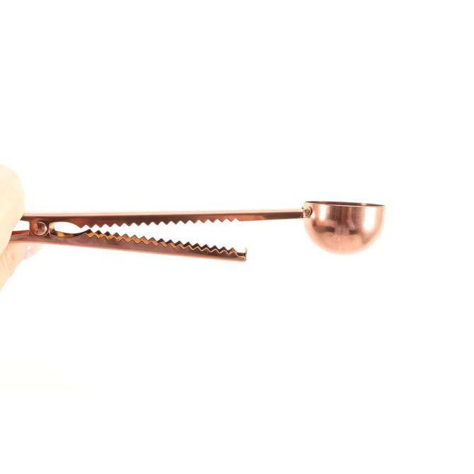 A copper coffee measuring spoon with a clip, featuring a curved scoop and textured grip for convenience.