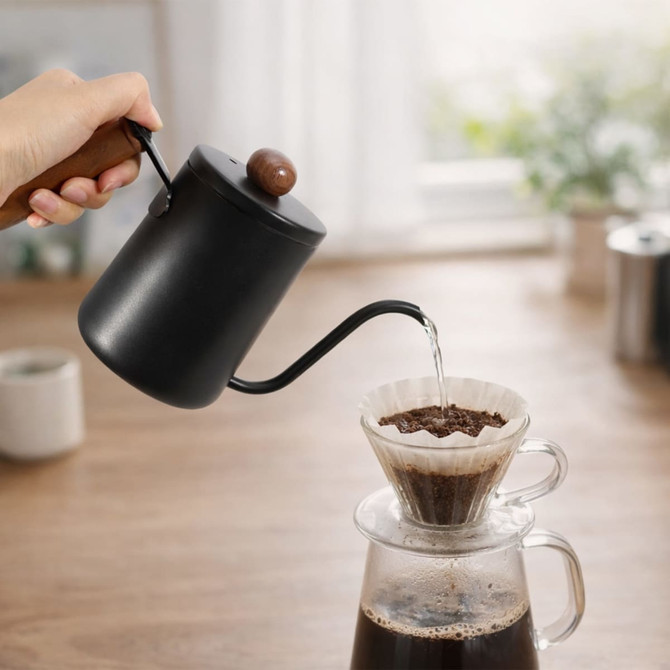 A stainless steel pour over kettle with a wooden handle in black, pouring water into a coffee filter.