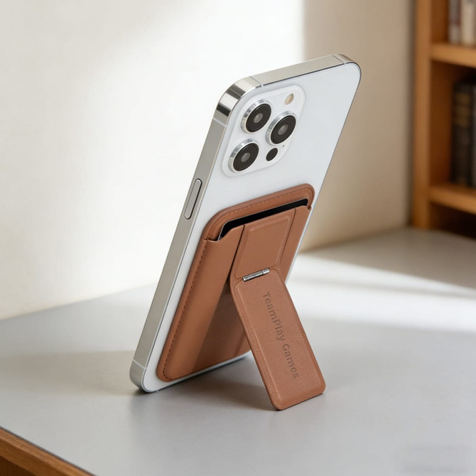 A brown PU magnetic card holder with a phone stand attached to a smartphone, placed on a table near a bookshelf.