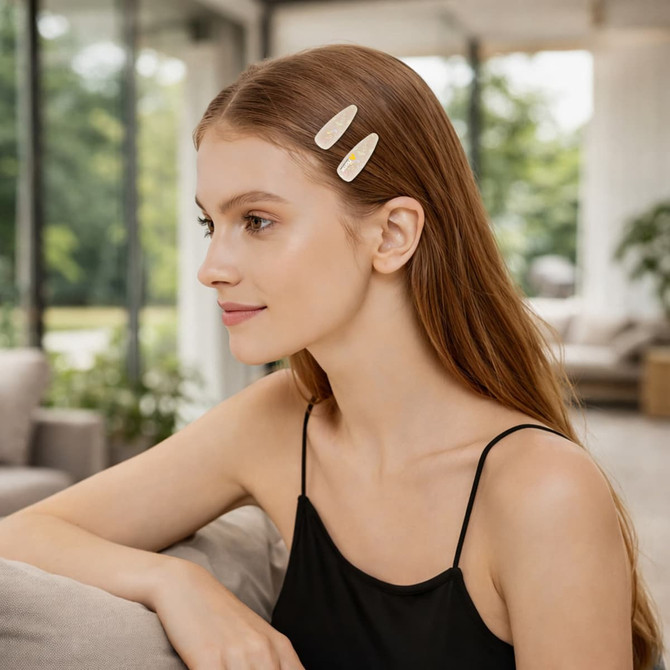 A model with long, straight brown hair wears two beige acetate hair alligator clips in her hair, set against a bright, airy background.