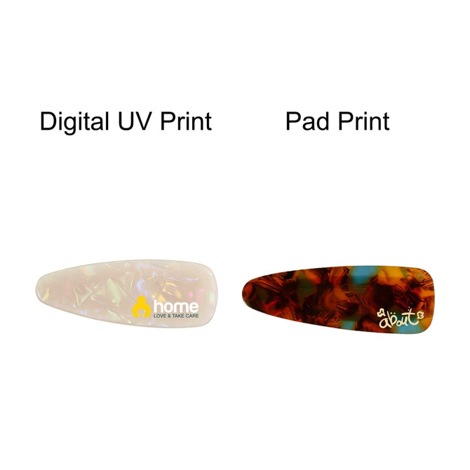 Two acetate hair alligator clips in different designs: one in a translucent white with a logo and one in a dark amber pattern.