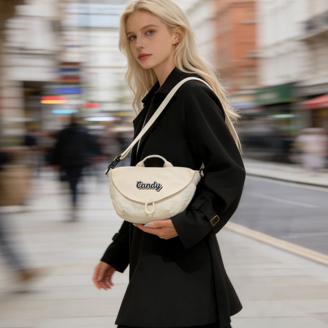A woman in a black coat carries a cream crossbody bag with a logo. The background features a blurred urban scene.