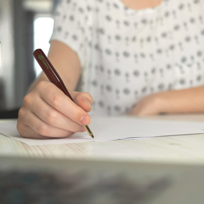 A brown pen with a baseball bat shape in use by a person writing on a sheet of paper.
