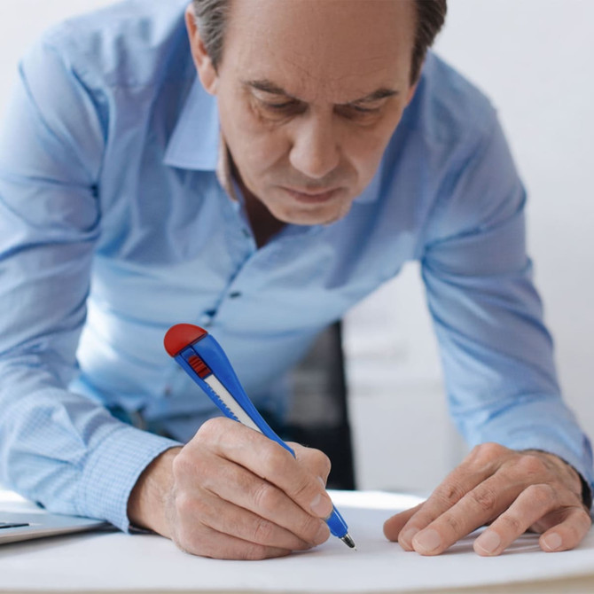 A blue and red knife-shaped ballpoint pen being used by a man in a light blue shirt while writing on paper.