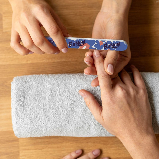 A sandpaper nail file in blue with a patterned design being used on a person's nails, placed on a grey towel.