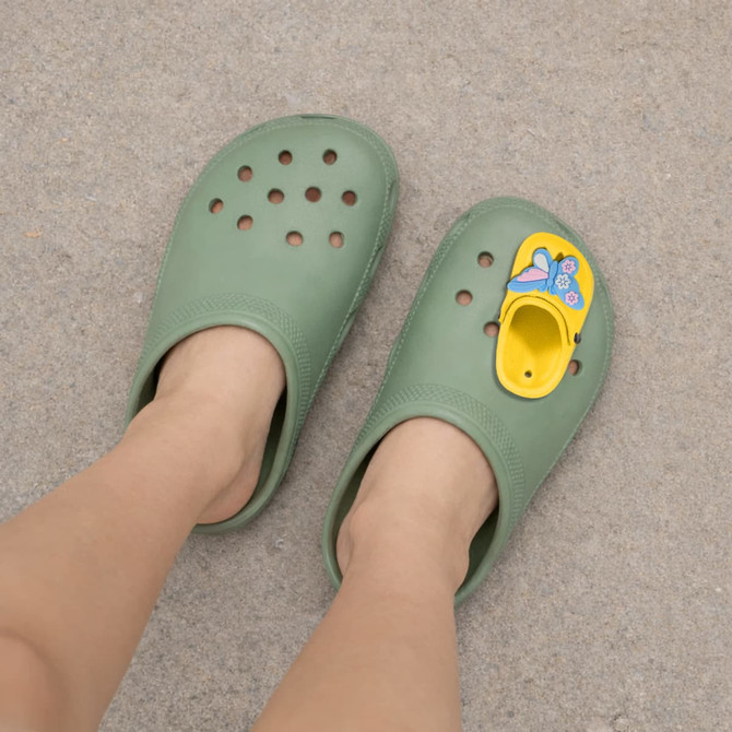 A pair of green clog shoes featuring a yellow paw-shaped charm on one side.