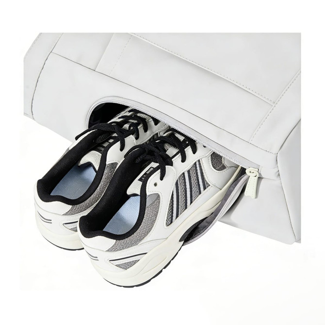 A lightweight tennis tote bag in white with a zippered compartment holding a pair of sneakers. It features a logo.